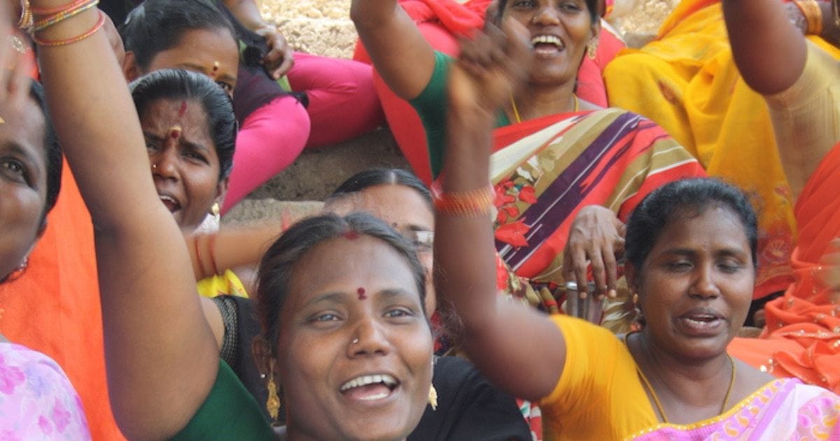 group of women in vibrant traditional clothing, raising their hands in the air with smiles, appearing energetic and joyful.