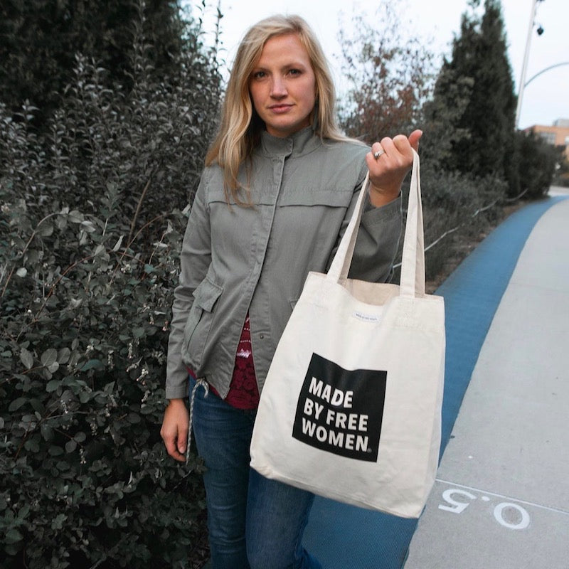 A woman proudly holds a tote bag labeled "Made by Free Women", showcasing freedom for women through ethical jobs..