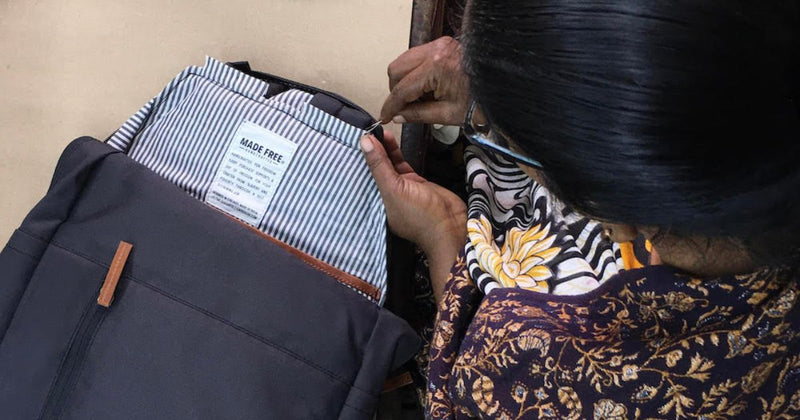 Person sewing a label onto striped fabric next to a black backpack.