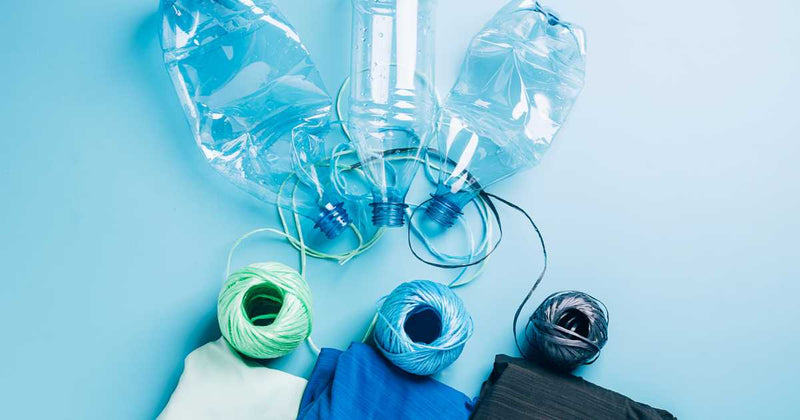 A collection of used plastic bottles, strings, and pieces of cloth on a light blue background. The plastic bottles are crushed, and the strings and cloth appear sorted by color. The scene emphasizes recycling and repurposing materials.