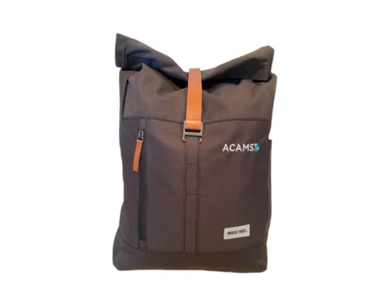 A dark gray roll-top backpack with a leather strap, ACAMS logo, and MADE FREE label on the front.