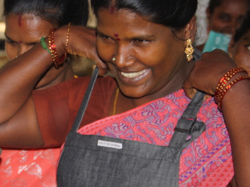 Smiling artisan puts on a 'Made by Free Women' apron, symbolizing ethical employment and empowerment.