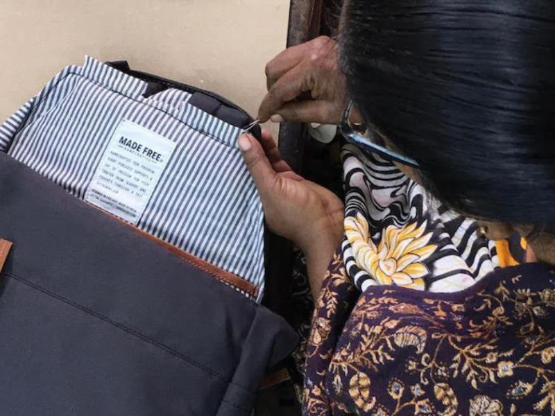 A close-up of an artisan hand-stitching a MADE FREE label inside a striped fabric bag, showing intricate craftsmanship.